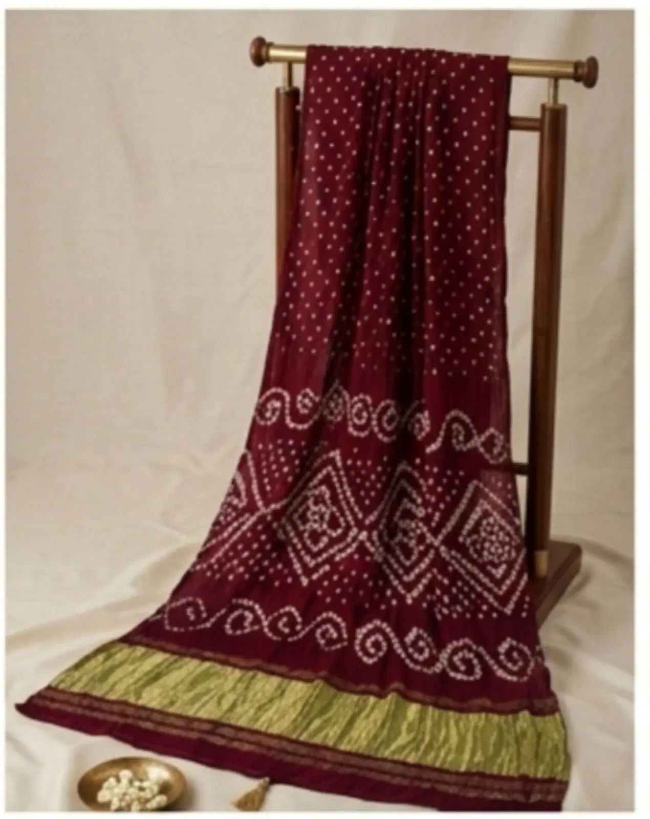 Maroon Bandhani-style saree with white dotted motifs and green border draped on a wooden stand