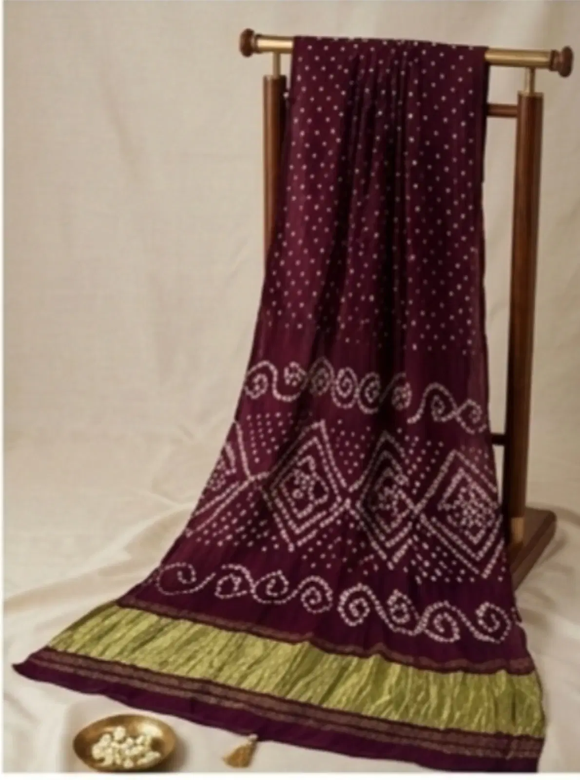 Maroon printed saree with white dotted motifs and green border draped on a wooden stand