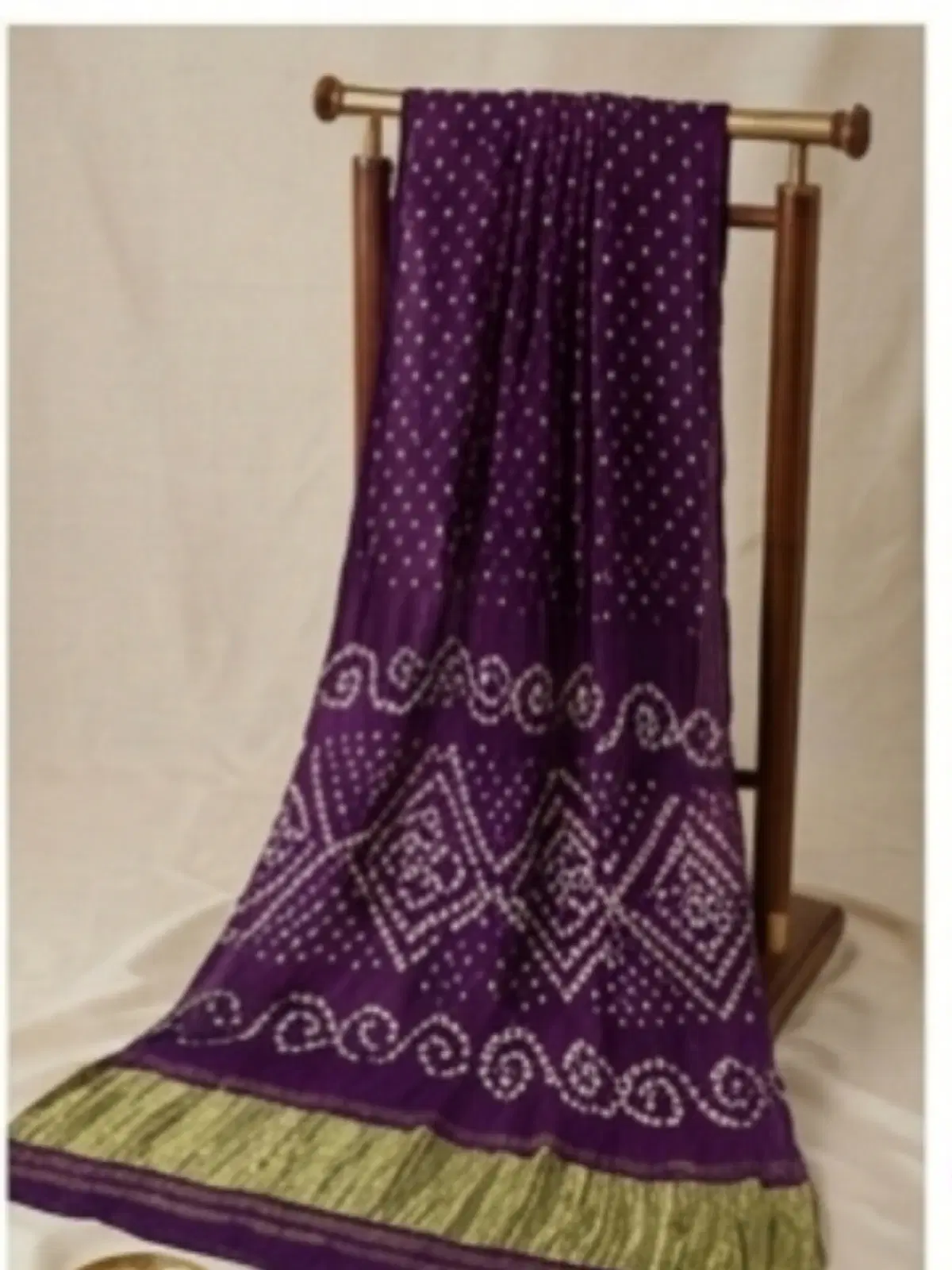 Purple printed saree with white dotted motifs and green border draped on a wooden stand