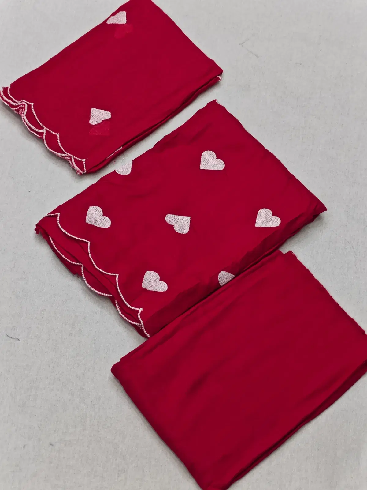 Folded red saree fabric set with white heart motifs and scalloped embroidered border