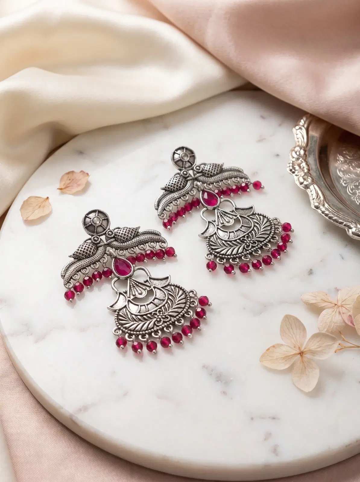 Pair of oxidised silver-tone statement earrings with pink beads and floral detailing on a marble surface