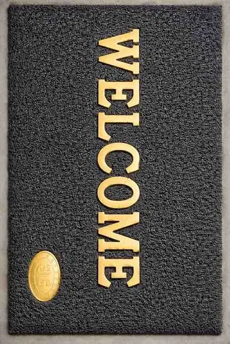 Rectangular dark welcome doormat with gold WELCOME text and oval gold emblem in one corner