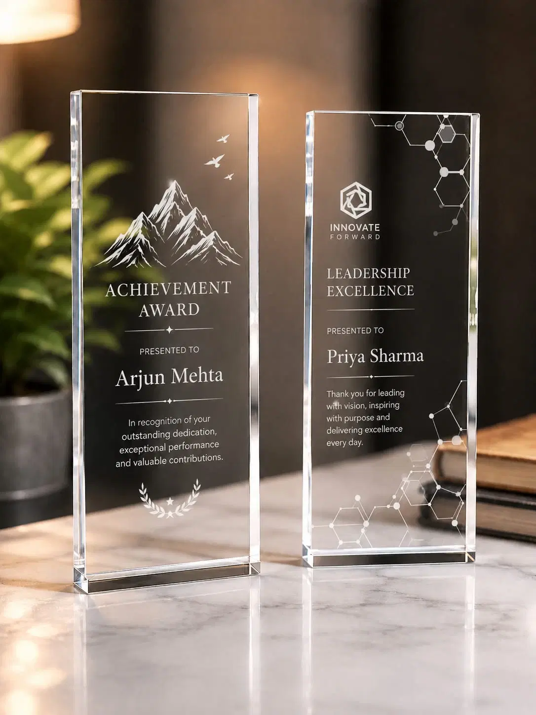 Two clear acrylic engraved award plaques displayed on a marble table