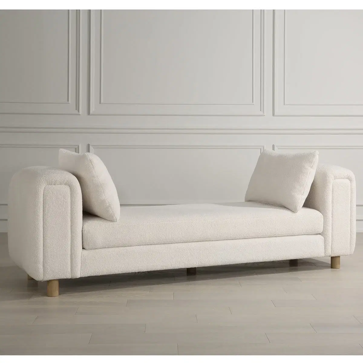 Front angled view of an ivory boucle sofa with rounded arms, wood feet, and two matching pillows