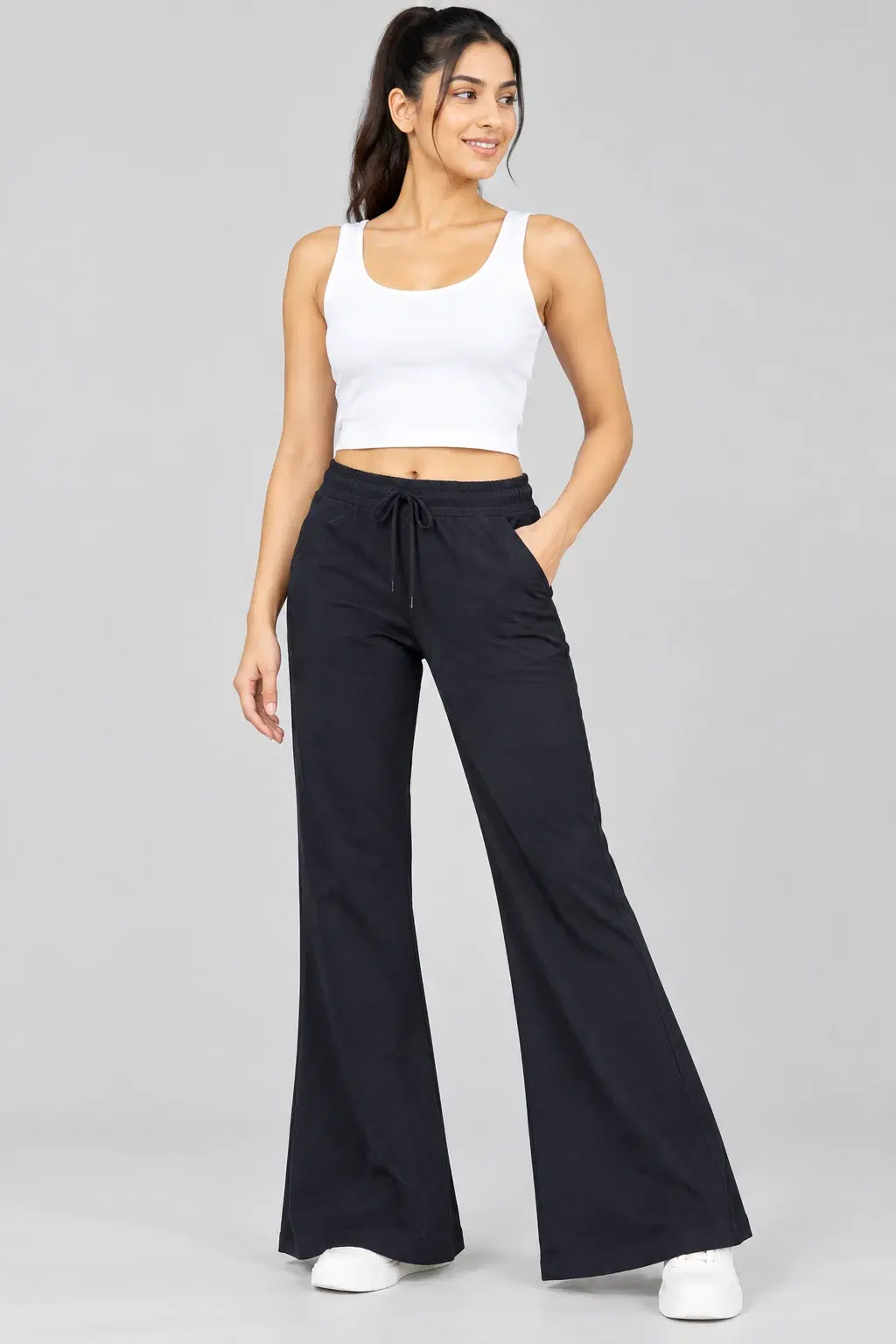 Black wide-leg drawstring pants shown on model with hand in pocket, paired with a white cropped tank