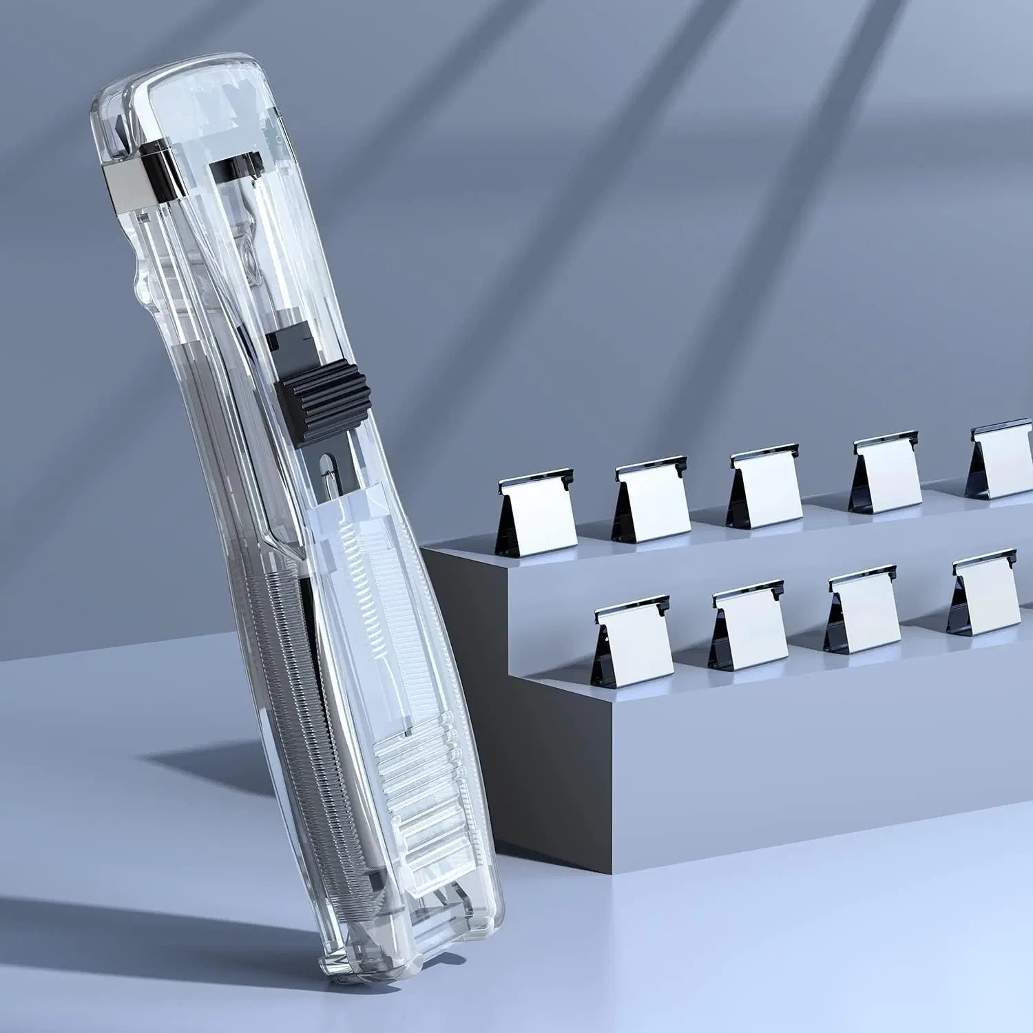 Transparent handheld staple-free stapler standing upright beside small silver refill clips
