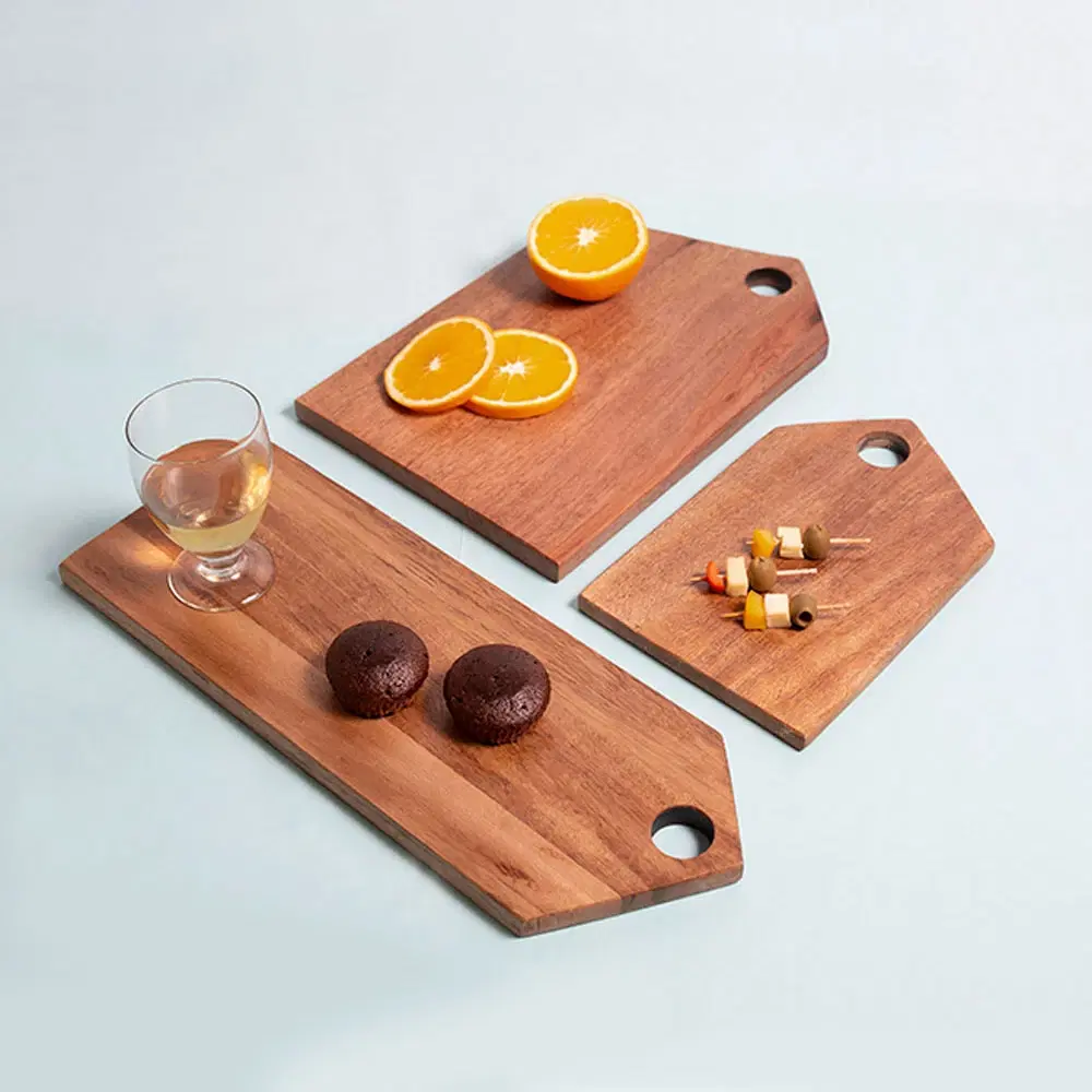 Three acacia wood serving boards styled with oranges, skewers, muffins and a glass on a light background