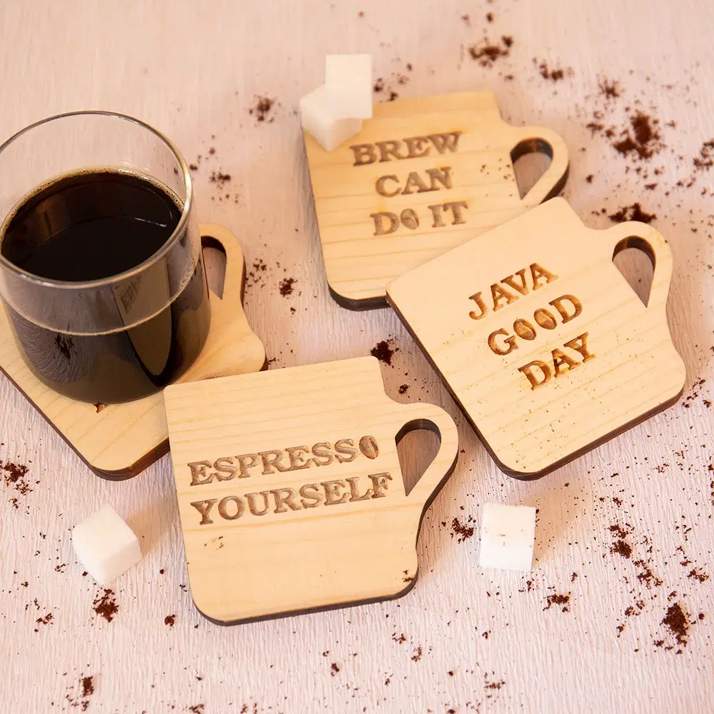 Four mug-shaped wooden coasters styled with a glass of black coffee, sugar cubes and coffee grounds