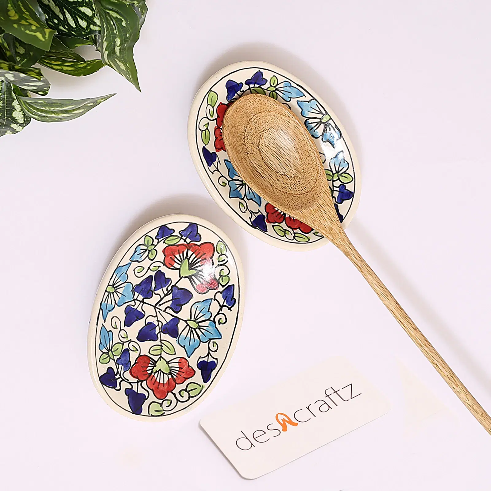 Two oval floral ceramic spoon rests displayed flat, with a wooden spoon placed on one piece. Dimension -  3.5'' x 4'' x 1''