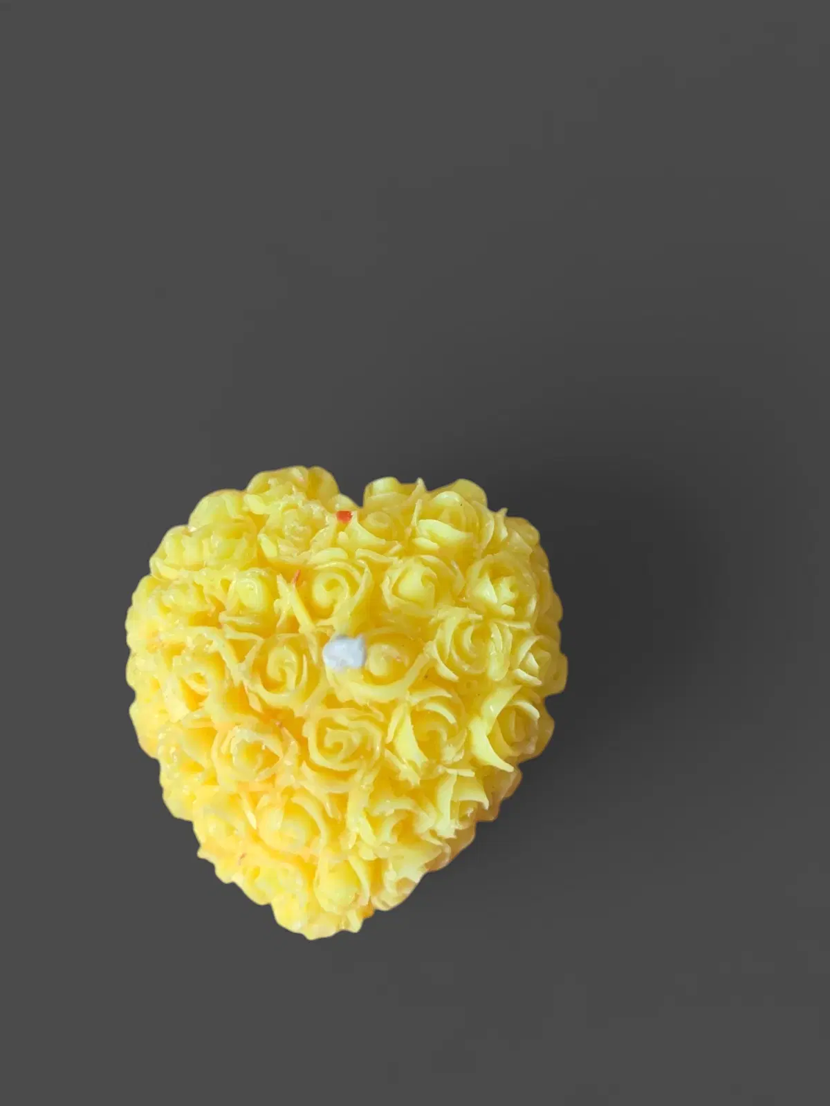 Top view of a yellow heart-shaped candle with rose detailing on a maroon fabric background