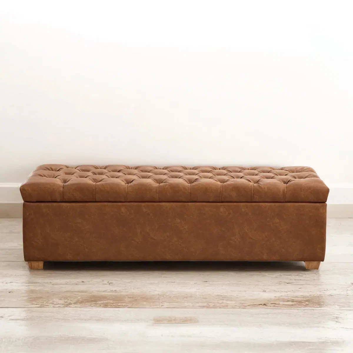 Front view of the closed tufted brown bench with wooden feet on a light floor
