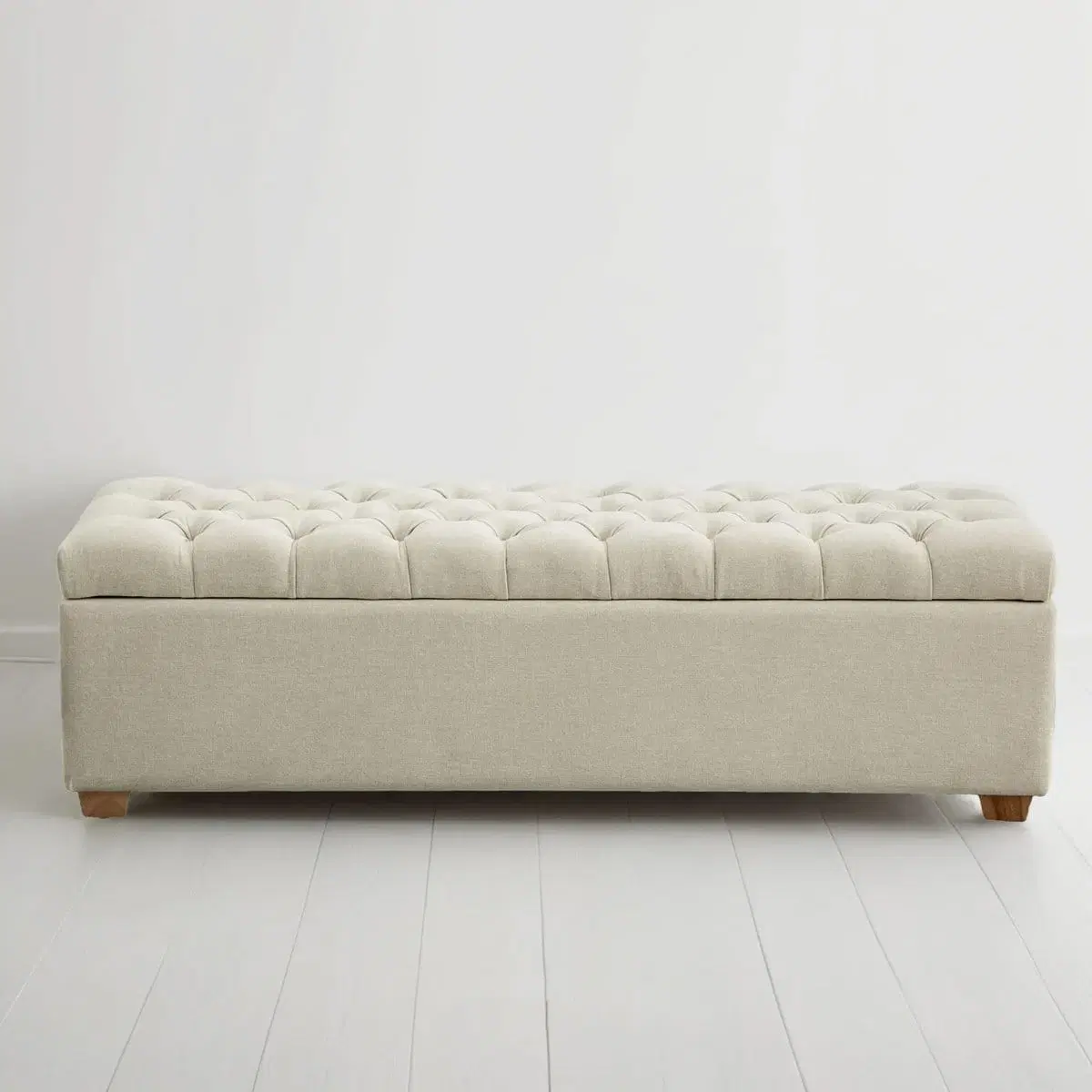 Front view of beige tufted storage bench with low wooden feet on a white floor