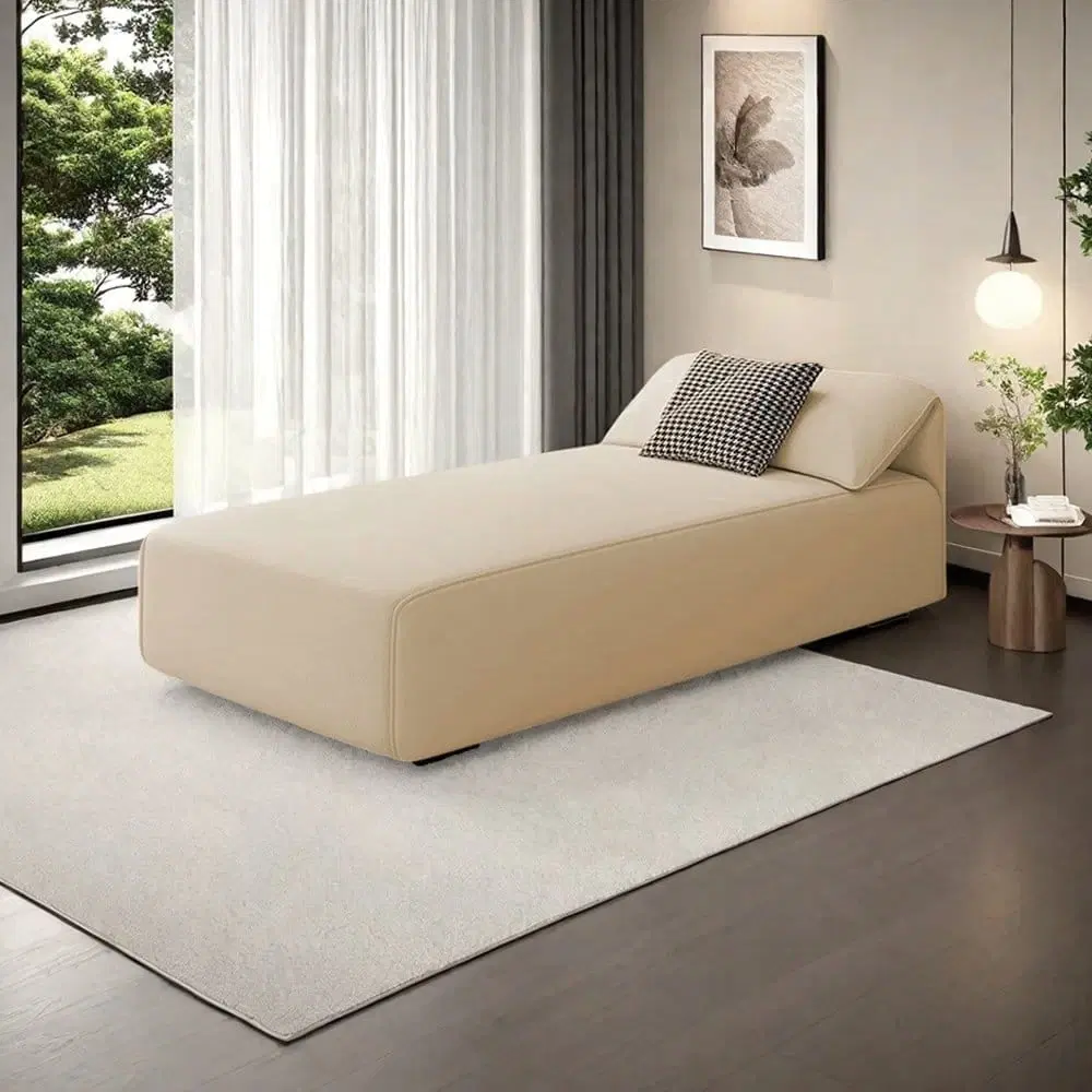 Cream upholstered chaise lounge with angled backrest styled in a modern bedroom beside a window