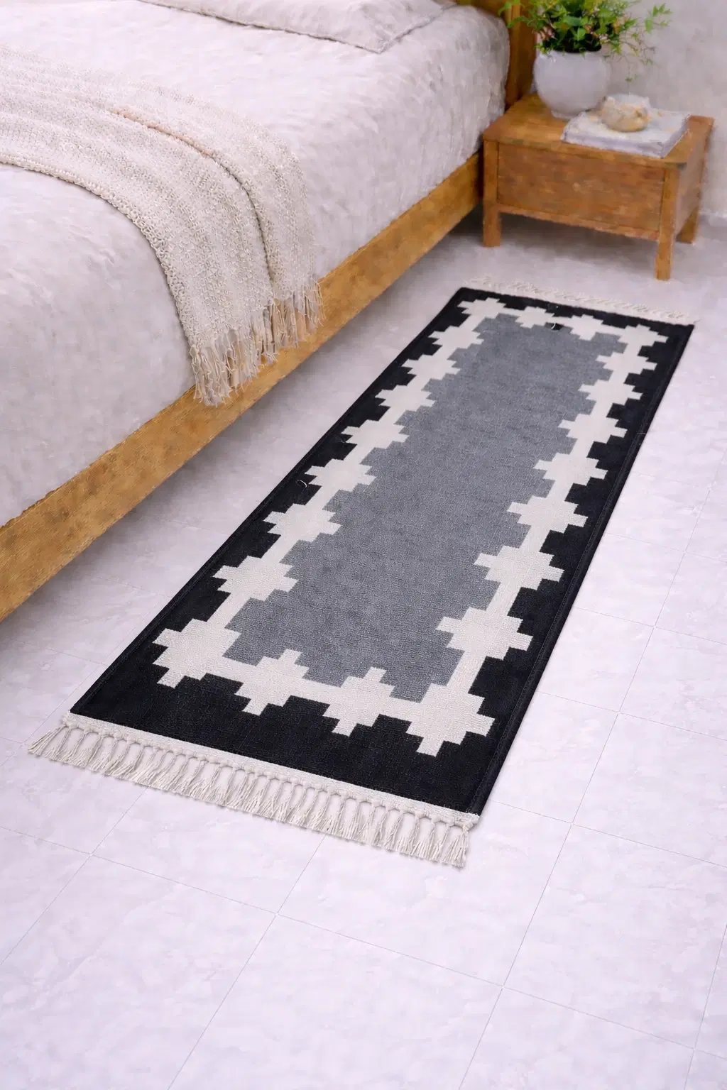 Black, white and grey geometric runner rug with tassel fringe placed beside a wooden bed