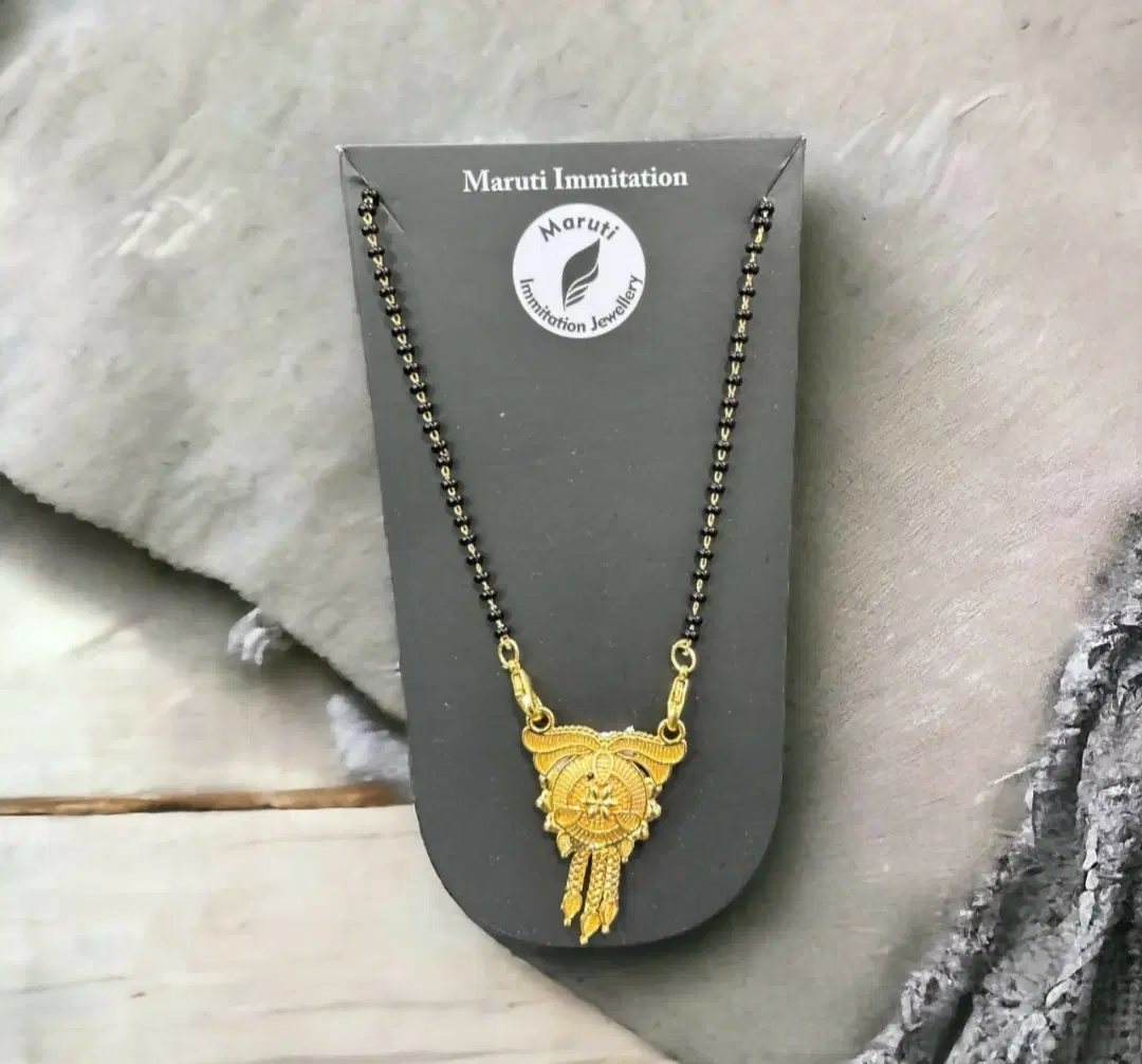 Front view of black beaded mangalsutra on display card with ornate gold-tone pendant