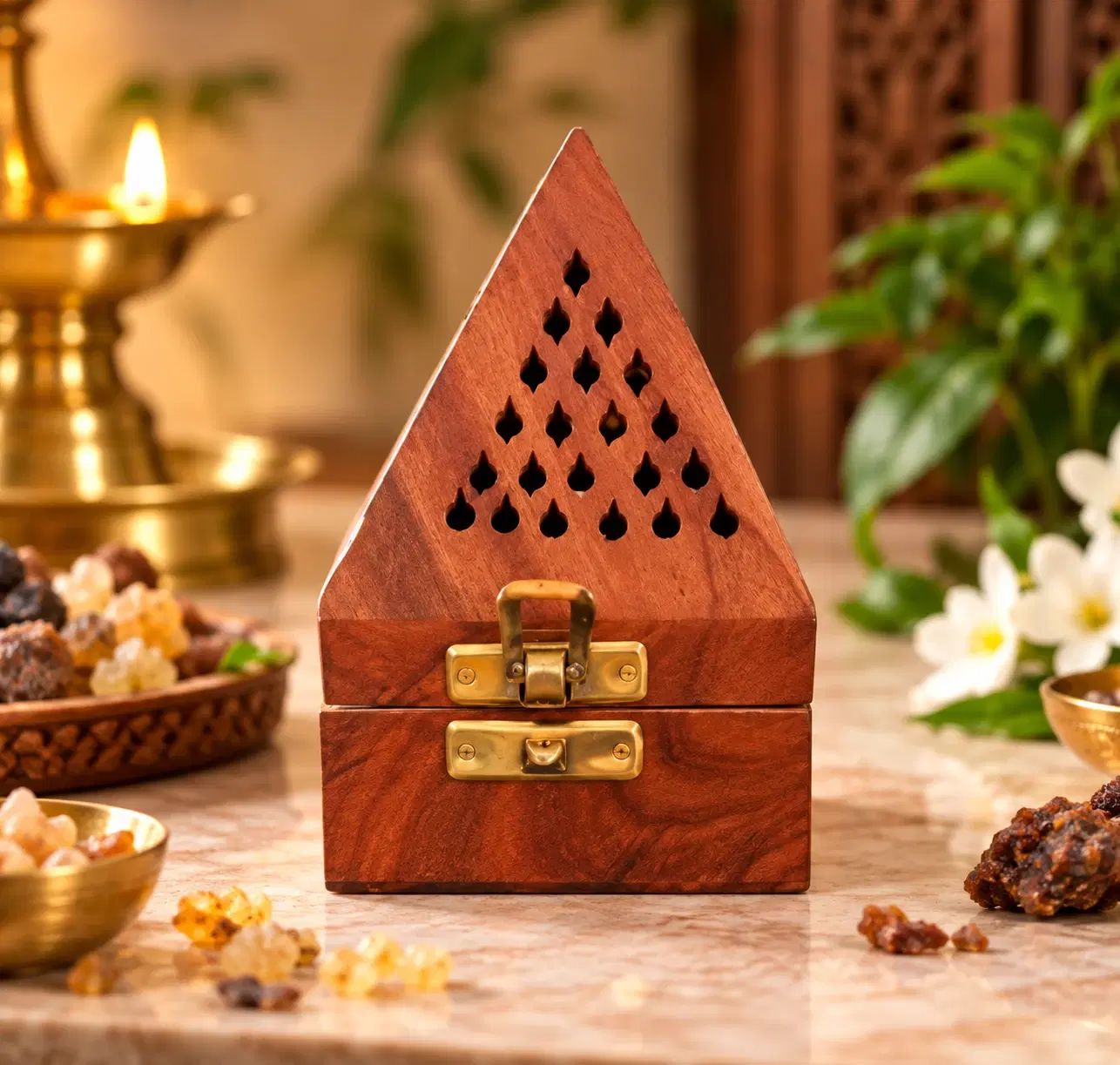 Front view of triangular wooden incense holder box with cutout vents and brass latch on a marble surface