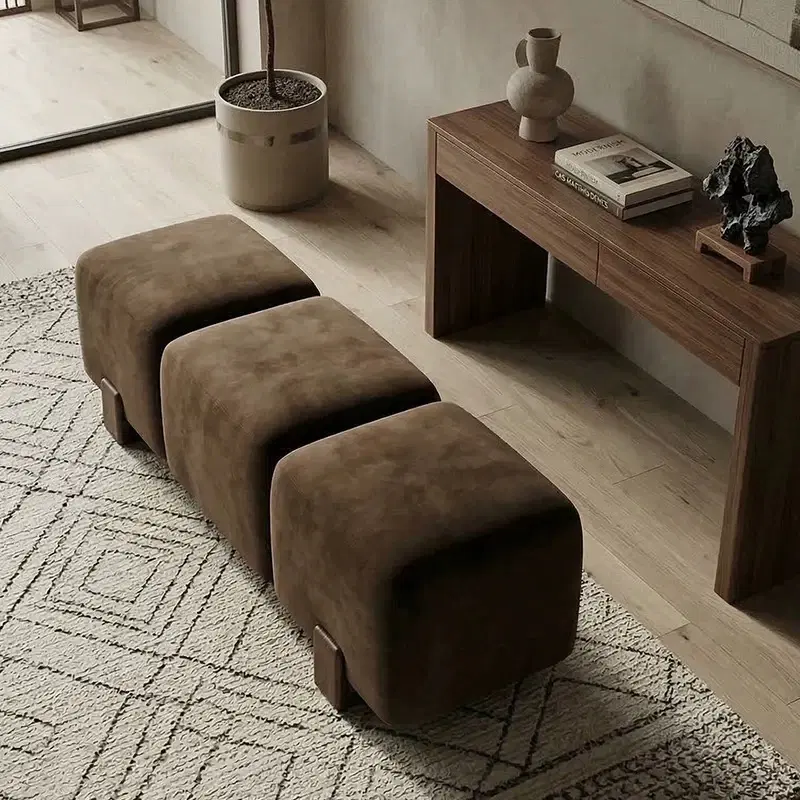 Brown three-section upholstered bench with rounded corners placed on a textured rug beside a wooden console