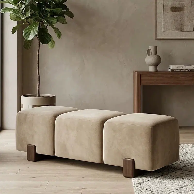 Beige upholstered three-section bench ottoman with rounded edges and dark wooden legs in a styled room
