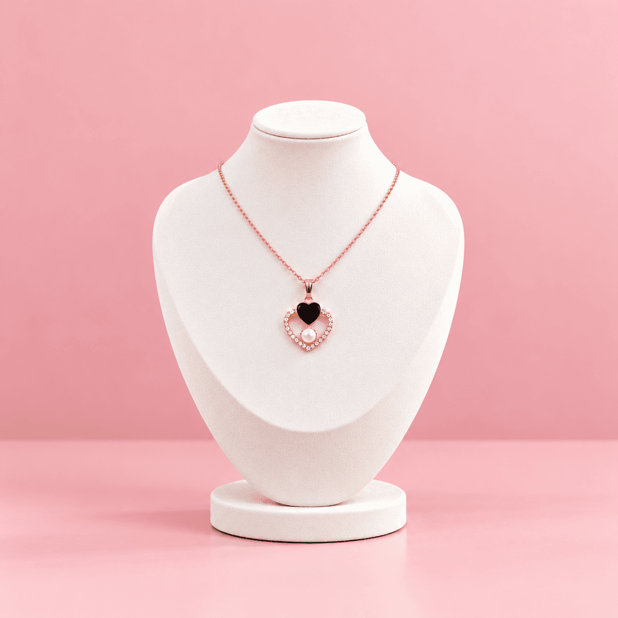 Rose gold necklace on white bust with crystal heart pendant, black heart accent and pearl on pink backdrop