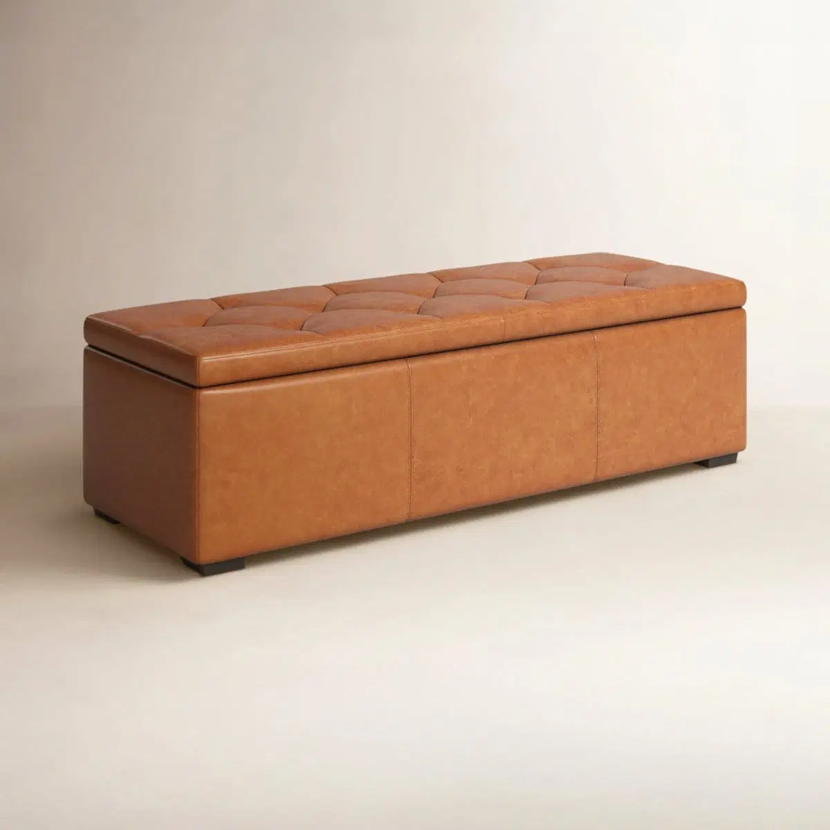 Angled front view of Lakeport cognac tan genuine leather storage ottoman with tufted lid and dark wood feet