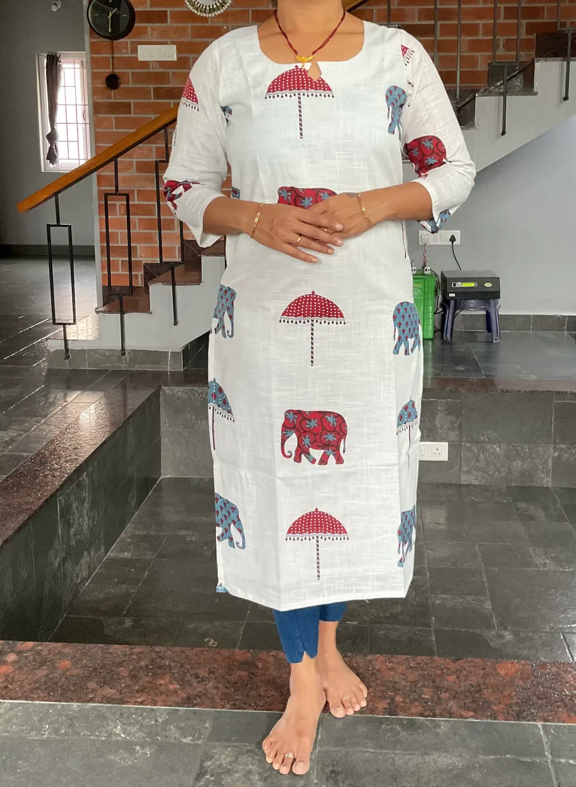 Woman wearing a white straight kurta with red and blue elephant and umbrella prints and 3/4 sleeves