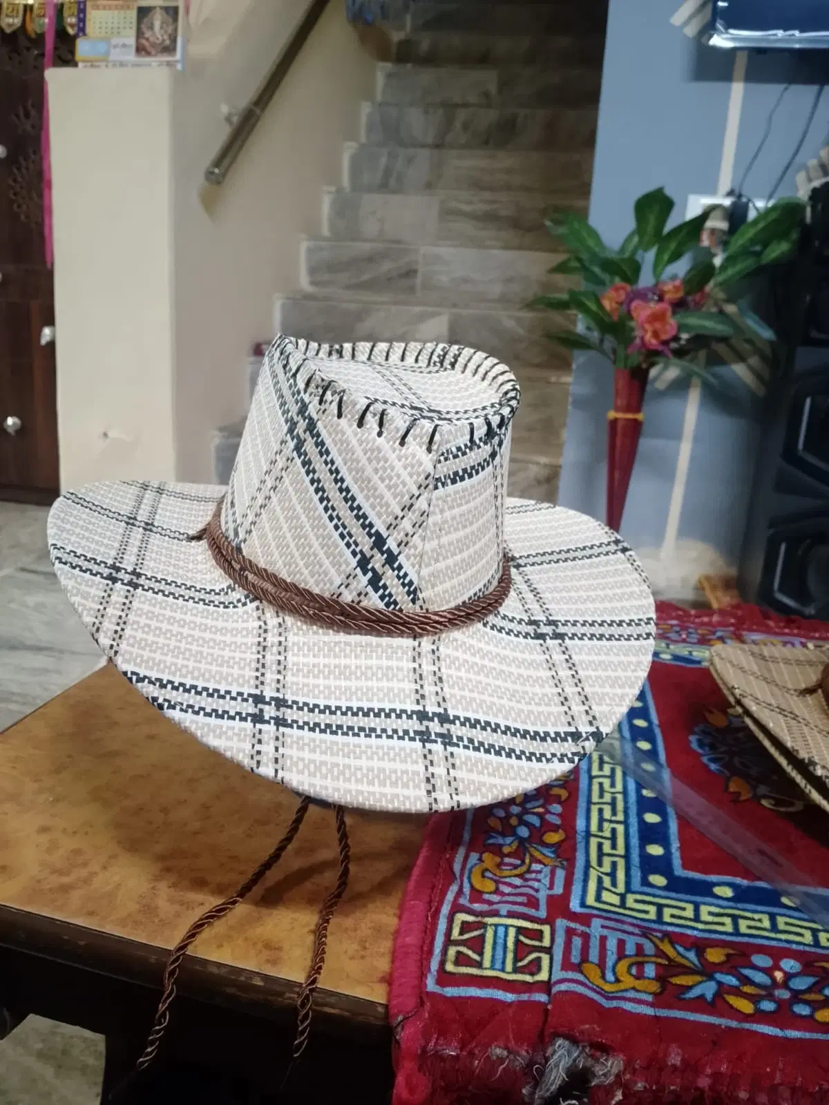 White woven cowboy hat with black plaid pattern and brown braided band on a table