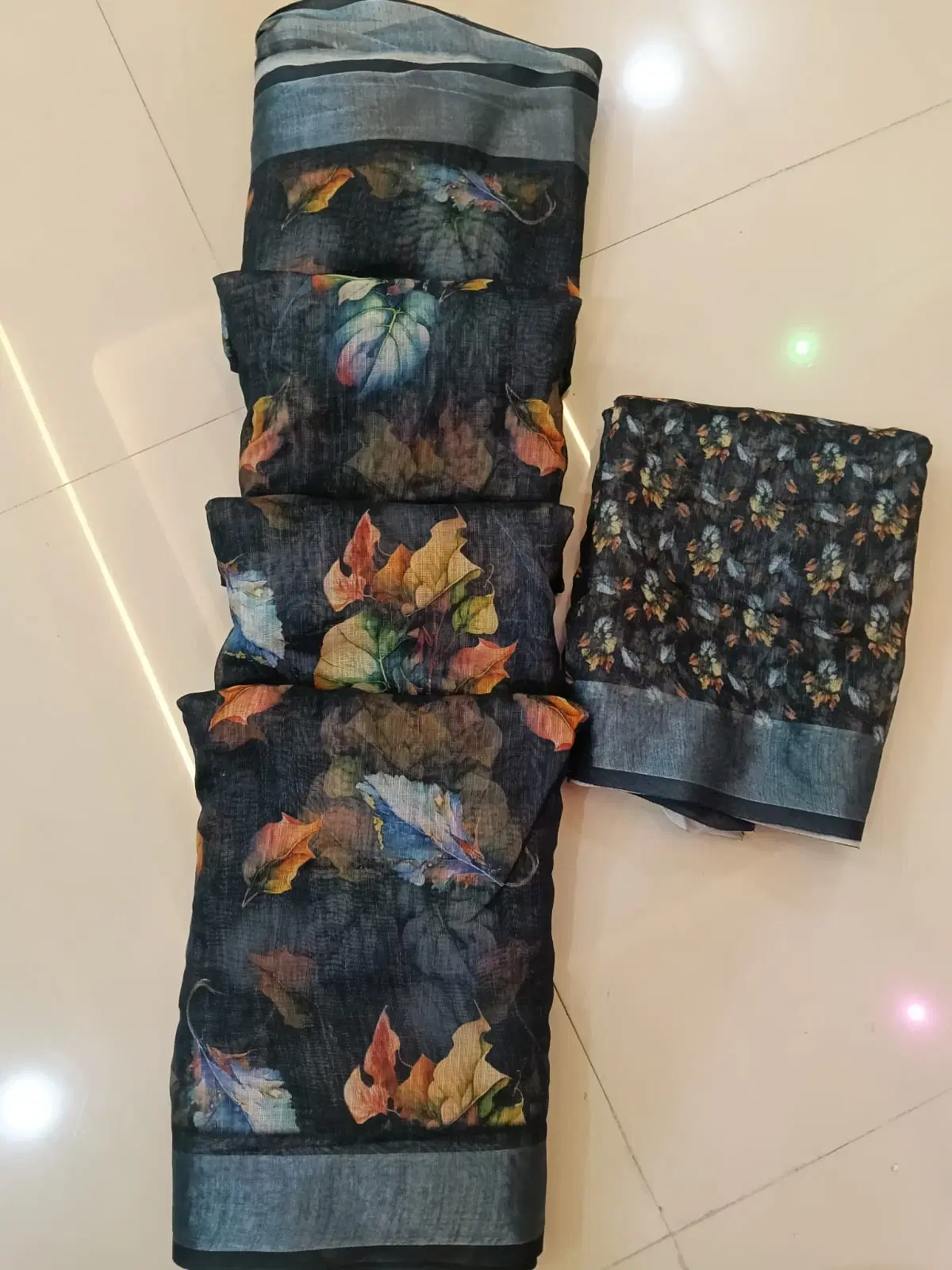 Dark floral printed saree fabric with matching blouse piece laid on a tiled floor